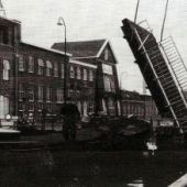 uit fotoarchief van Hilbrand de Vries - Boomend door de ophaalbrug in de Oliemolenstraat. Op de achtergrond de gebouwen van de huidige Dunlop